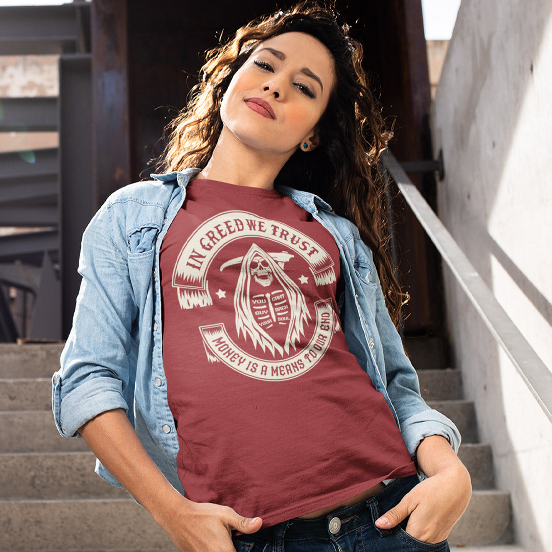 Woman wearing a maroon t-shirt with a graphic design and text, standing outdoors. A broken society t shirt implying we have made greed our new God. If you believe our obsession with money is lowering the standards of society, help create social awareness with this anti capitalism t shirt. Could it be that money worship will be the end of us ? Made from 100% organic ring-spun cotton, this broken society t shirt is unisex, high quality, super comfy, and best of all, eco-friendly.
