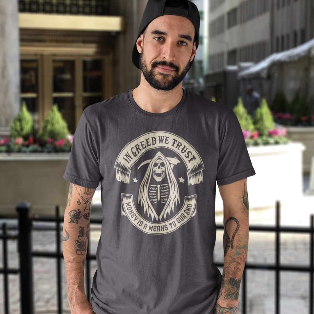 Man wearing a dark grey t-shirt with a graphic design and text, standing outdoors. A broken society t shirt implying we have made greed our new God. If you believe our obsession with money is lowering the standards of society, help create social awareness with this anti capitalism t shirt. Could it be that money worship will be the end of us ? Made from 100% organic ring-spun cotton, this broken society t shirt is unisex, high quality, super comfy, and best of all, eco-friendly.