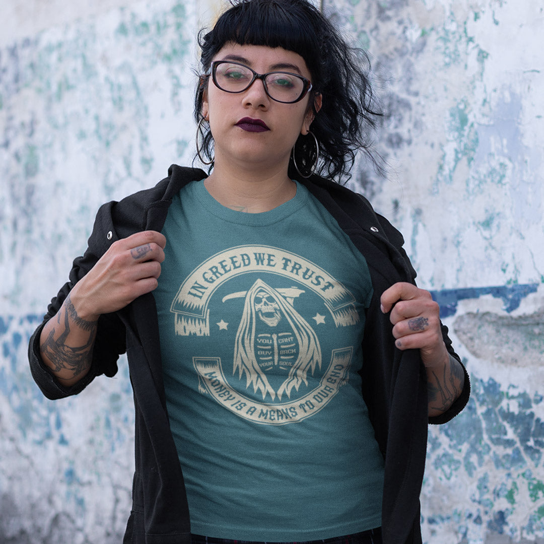 Person wearing a teal t-shirt with a graphic design and text, standing against a textured wall. A broken society t shirt implying we have made greed our new God. If you believe our obsession with money is lowering the standards of society, help create social awareness with this anti capitalism t shirt. Could it be that money worship will be the end of us ? Made from 100% organic ring-spun cotton, this broken society t shirt is unisex, high quality, super comfy, and best of all, eco-friendly.