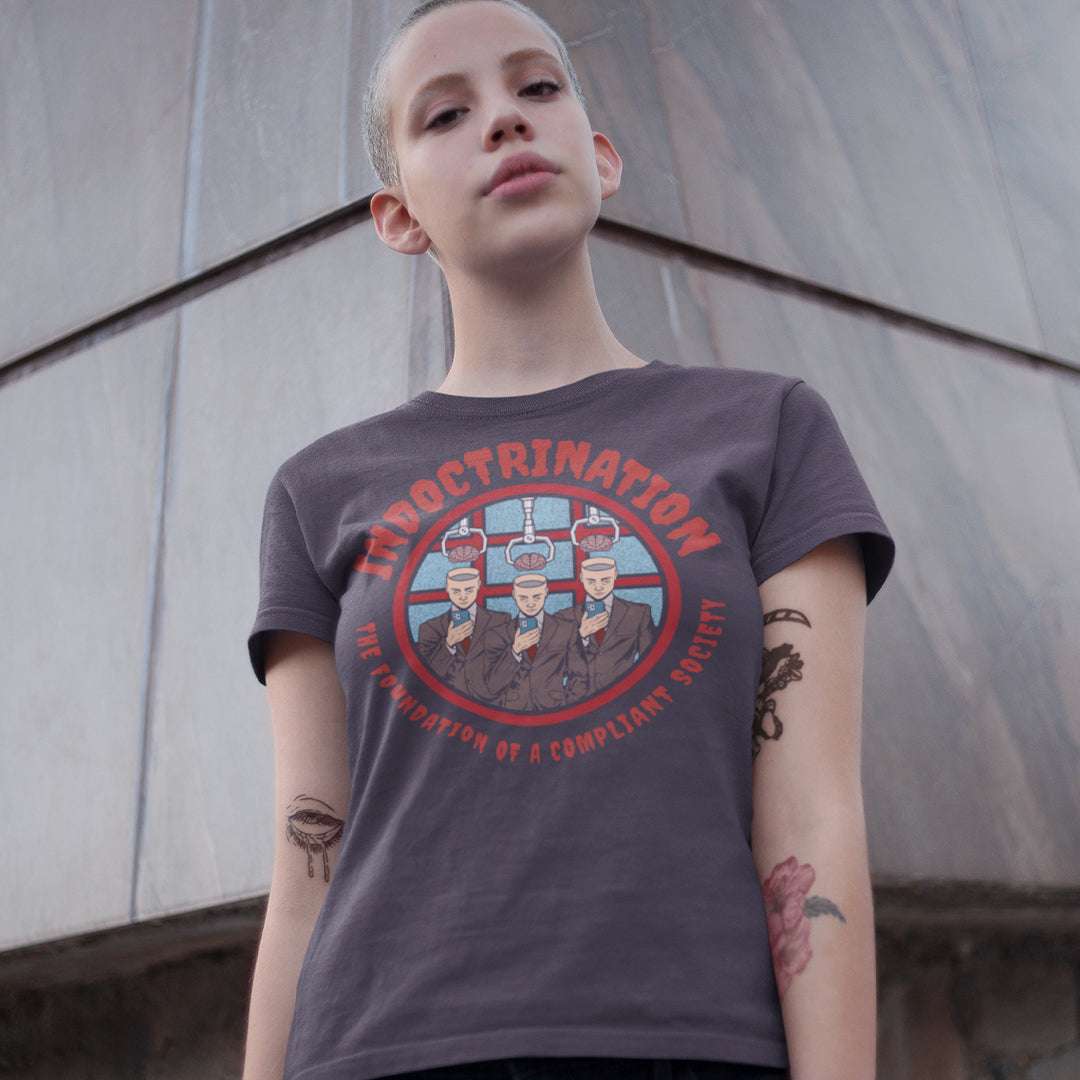 Person wearing a t-shirt with a graphic design and text, standing against a textured wall. A conspiracy theory t shirt exposing indoctrination as the foundation of modern society. What we believe before we realise we are being lied to shapes our lives until we take back our own opinions. Made from 100% organic ring-spun cotton, this non conformist t shirt is unisex, high quality, super comfy, and best of all, eco-friendly.