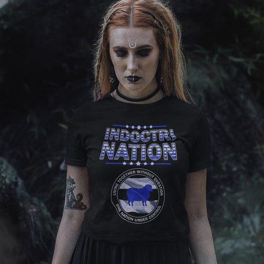 A gothic woman with piercings, standing outside, wearing a black short sleeved crew neck t-shirt with a logo of a sheep on a flag and the text "INDOCTRINATION" above it.