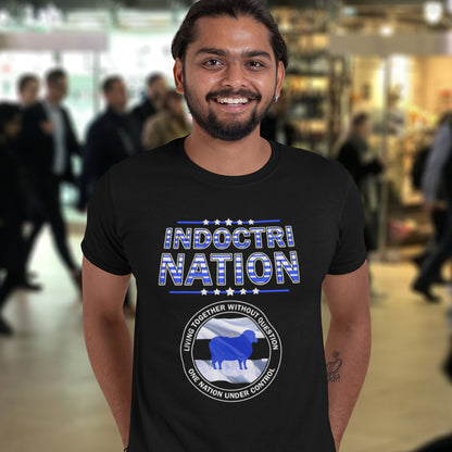 Man wearing a black t-shirt with 'INDOCTRI NATION' text and graphics in a blurred indoor setting. A non conformist t shirt with satirical look at nationalism, an insight into a very dark future for any nation under a controlling government. Display your social awareness with this unique design.  Made from 100% organic ring-spun cotton, this urban art t shirt is unisex, high-quality, super comfy, and best of all, eco-friendly.