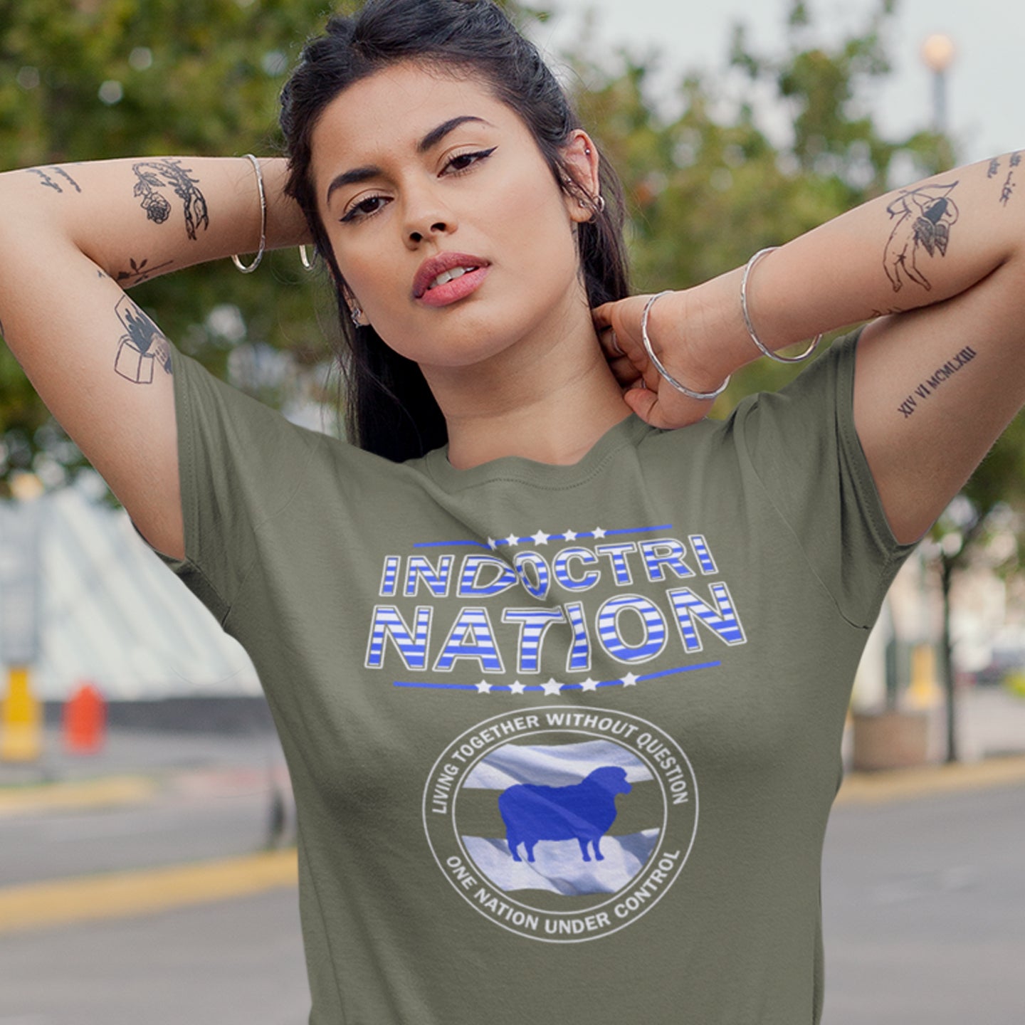 Woman wearing a green t-shirt with 'Indoctrination' text and logo outdoors. A political t-shirt with satirical look at nationalism, an insight into a very dark future for any nation under a controlling government. Display your social awareness with this unique design. Made from 100% organic ring-spun cotton, this political t-shirt is unisex, high-quality, super comfy, and best of all, eco-friendly.