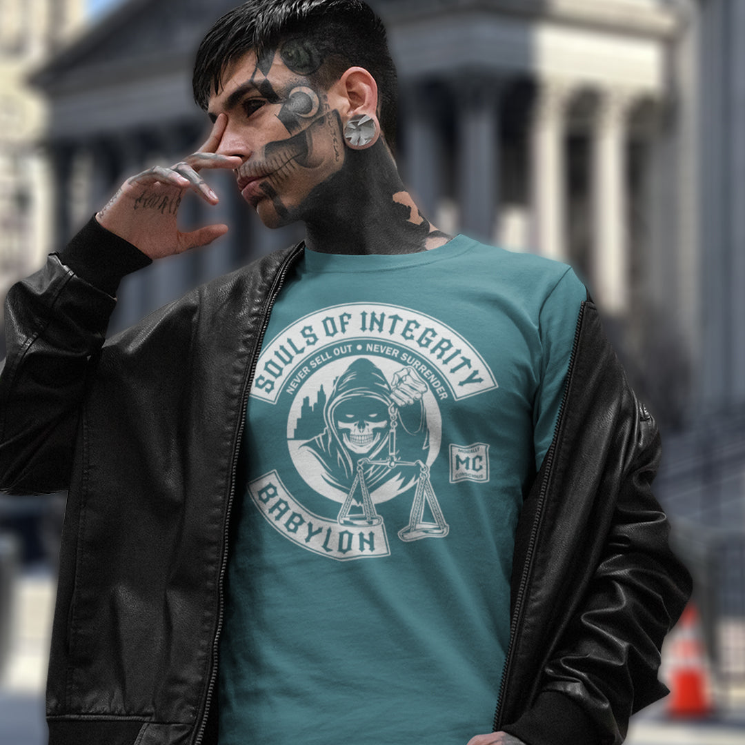 Man wearing a teal t-shirt with a graphic design and text, standing outdoors. A social awareness t shirt promoting ethics and morality. A spoof motorcycle club design for people who still have integrity. This design satirically representing how few people are left with a moral conscience in a corrupt world, or as the Rastafarians call it, BABYLON. Made from 100% organic ring-spun cotton, these social issues t shirts are unisex, high-quality, super comfy, and best of all, eco-friendly.