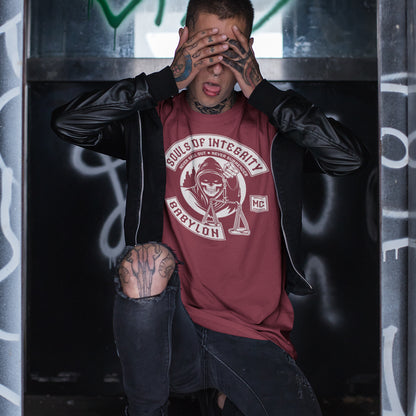 Person wearing a 'Souls of Integrity' t-shirt with tattoos in front of a graffiti-covered wall. A social awareness t shirt promoting ethics and morality. A spoof motorcycle club design for people who still have integrity. This design satirically representing how few people are left with a moral conscience in a corrupt world, or as the Rastafarians call it, BABYLON. Made from 100% organic ring-spun cotton, these social issues t shirts are unisex, high-quality, super comfy, and best of all, eco-friendly.