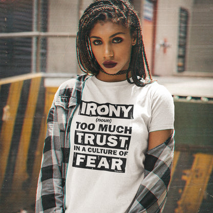 A woman wearing a white graphic t-shirt with bold black text that reads 'IRONY (noun) TOO MUCH TRUST IN A CULTURE OF FEAR', styled with a black-and-white plaid shirt draped off her shoulders in an urban setting.