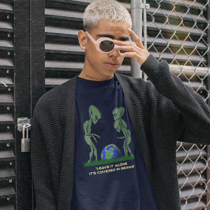 A person wearing a French navy graphic t-shirt with a green alien design and text, styled with a black knit cardigan and light pink sunglasses, standing in front of a black metal gate and chain-link fence.