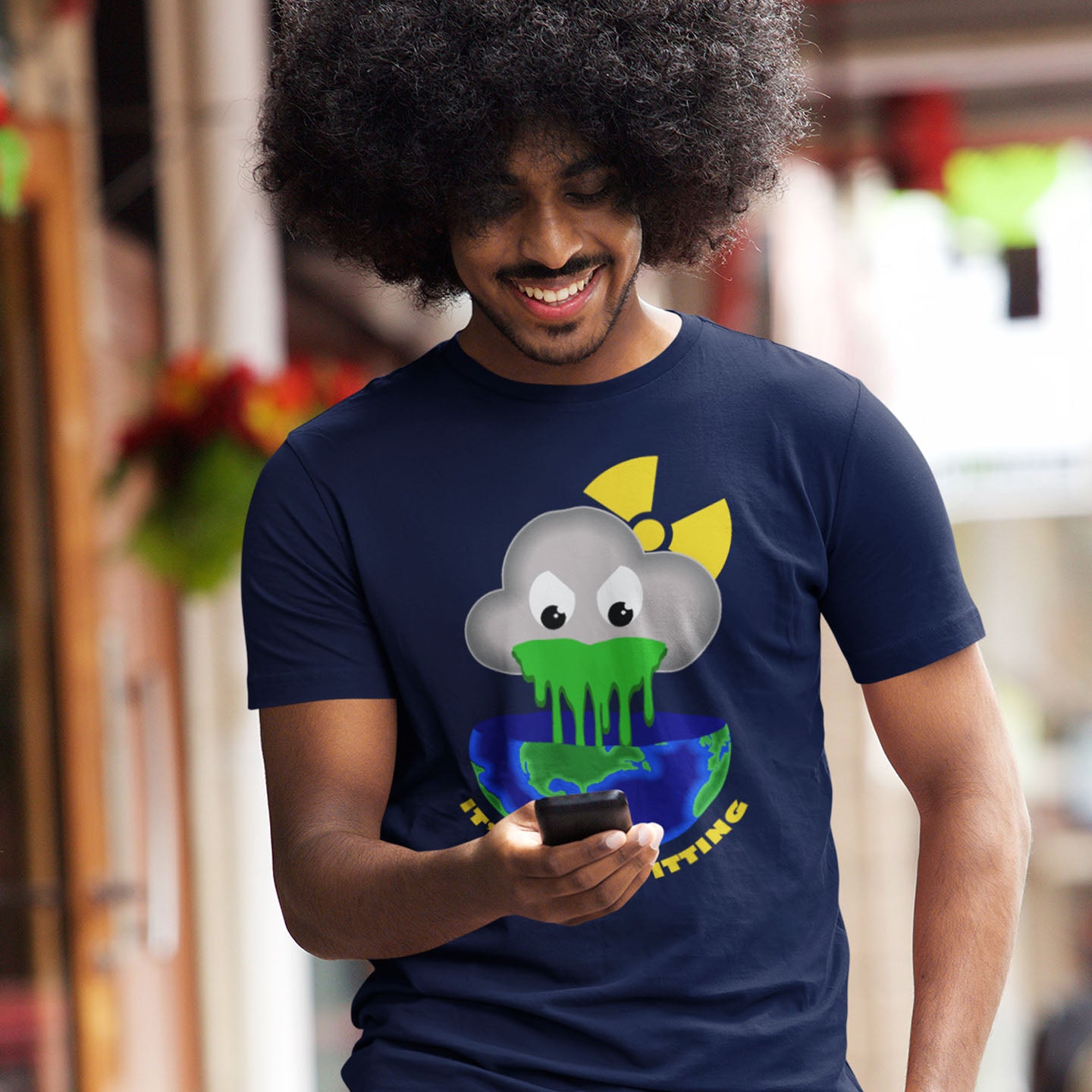 Man wearing a French navy blue t-shirt with a graphic design, holding a phone in an urban setting.