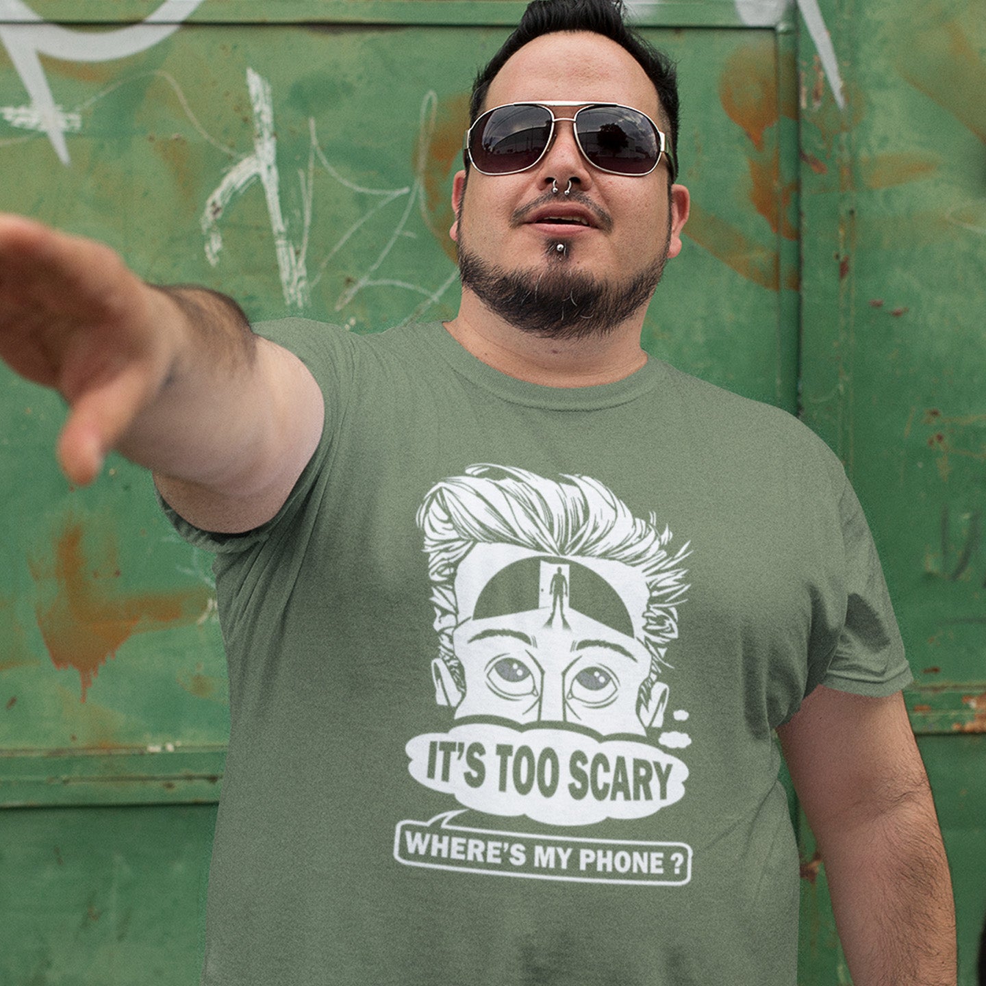 Man wearing a khaki t-shirt with a graphic design and text, standing against a green wall with graffiti. An anti-mobile phone abuse t-shirt highlighting the effects on the mind of smart phone over use in the place of thinking. A view of how mobile phones have taken over thinking and left us with dark unexplored corridors in our minds. Made from 100% organic ring-spun cotton, this social awareness t-shirt is unisex, high-quality, super comfy, and best of all, eco-friendly.