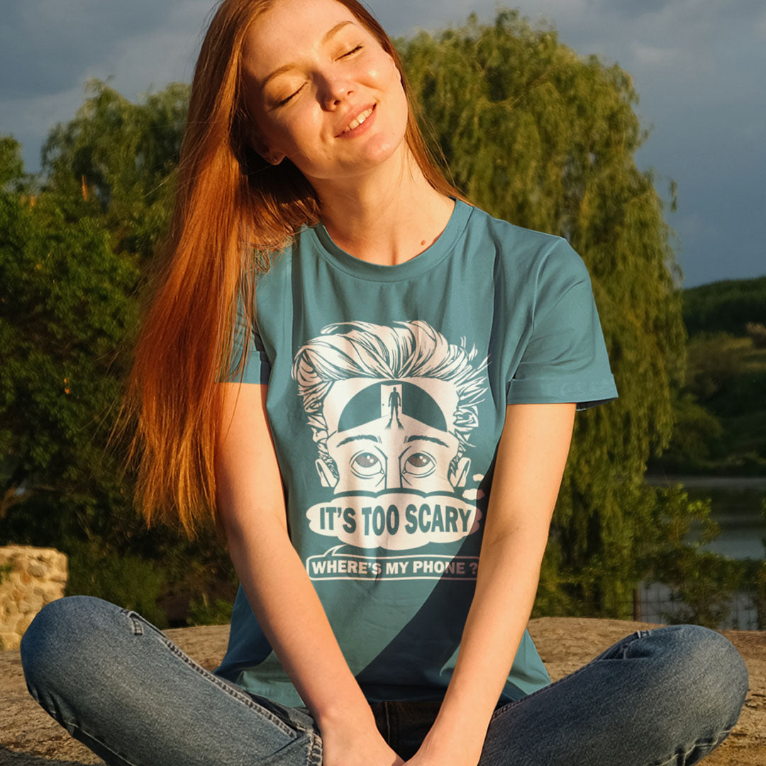 Person wearing a teal t-shirt with a graphic design sitting outdoors. An anti mobile phone abuse t-shirt highlighting the effects on the mind of smart phone over use in the place of thinking. A view of how mobile phones have taken over thinking and left us with dark unexplored corridors in our minds. Made from 100% organic ring-spun cotton, this social awareness t-shirt is unisex, high-quality, super comfy, and best of all, eco-friendly.