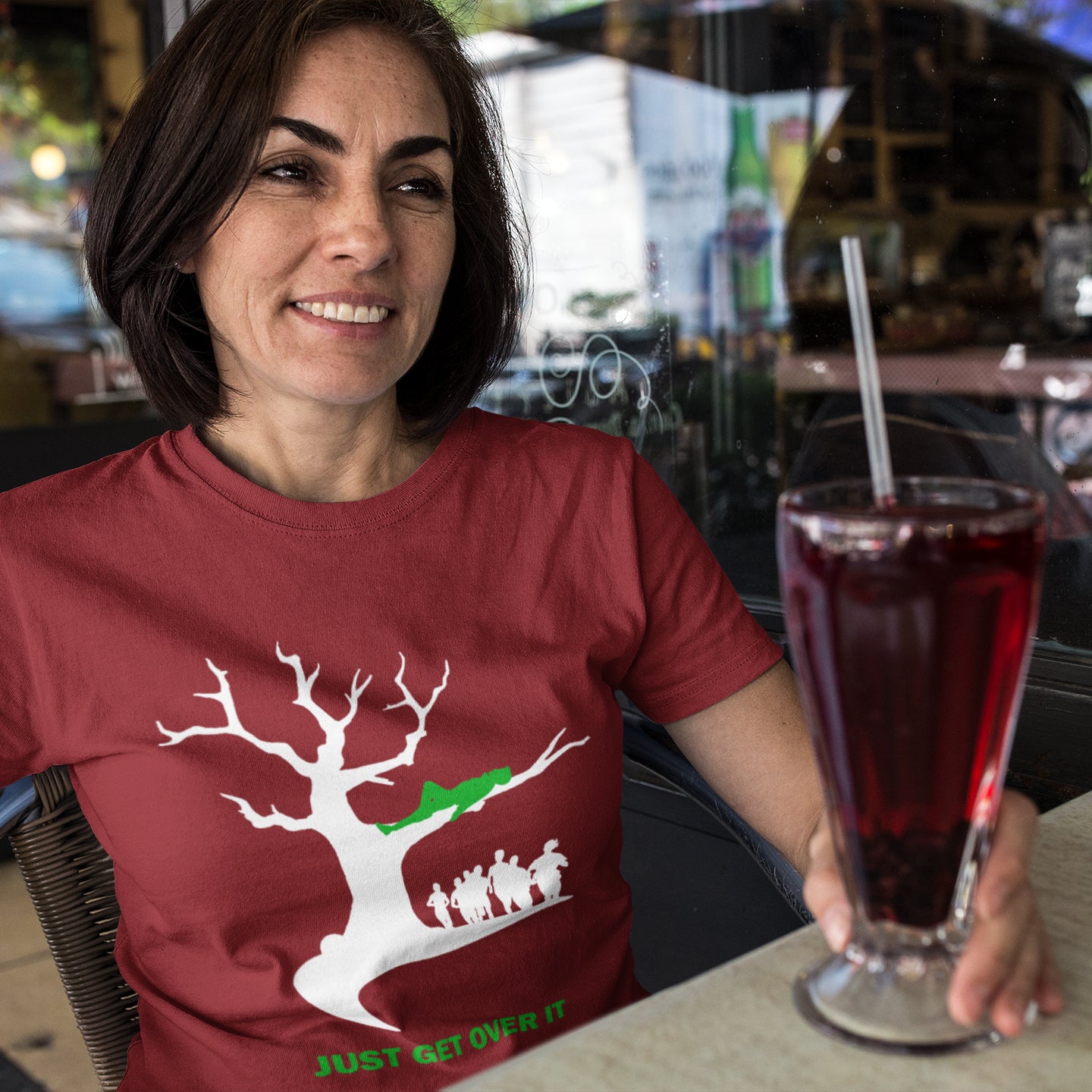 Woman wearing a burgundy t-shirt with a graphic design, sitting at a table with a drink. This sarcastic motivational t-shirt design is for everyone who doesn't need a motivational one liner to find their pace of life. Made from 100% organic ring-spun cotton, this underground stencil art t-shirt is unisex, high-quality, super comfy, and best of all, eco-friendly.
