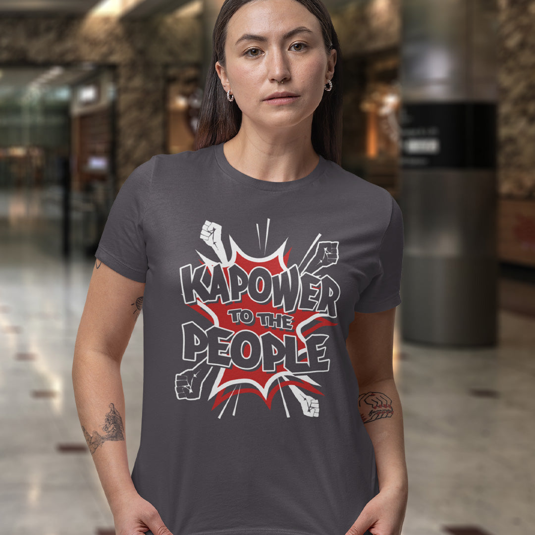 Person wearing a t-shirt with 'Kapower to the People' design in an indoor setting. This anti government t shirt packs a punch with this humorous play on the slogan 'Power to the people', with a comic book twist. Support true democracy with this funny political message. Made from 100% organic ring-spun cotton, this unisex non conformist t shirt is a total must-have. It's high-quality, super comfy, and best of all, eco-friendly