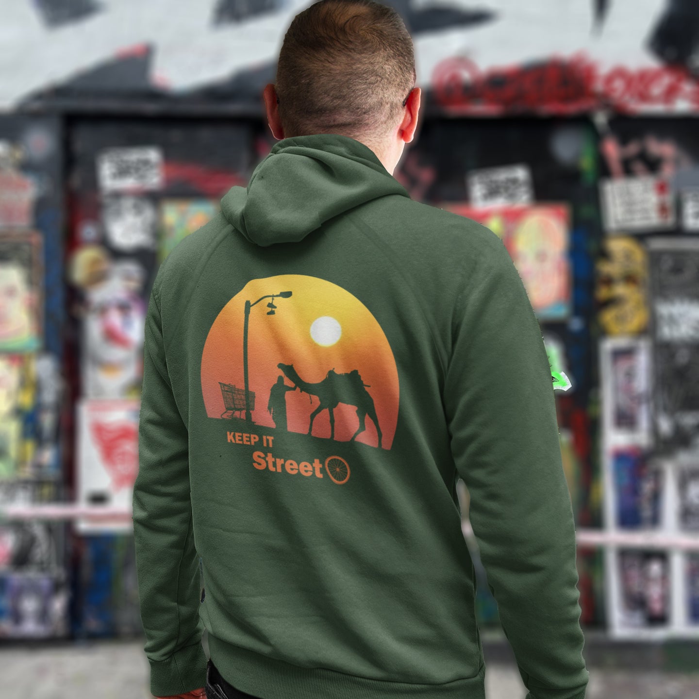 Person wearing a bottle green hoodie with a graphic design on the back, standing in front of a colourful store display. This street art inspired hoodie design represents inner city street life as a culture of it's own.  Wherever you are in the world, may the street be with you. Comfortable and practical. It's extra soft and has a convenient front pouch pocket. Made from organic cotton and recycled polyester, this street art hoodie is a great eco-friendly choice.
