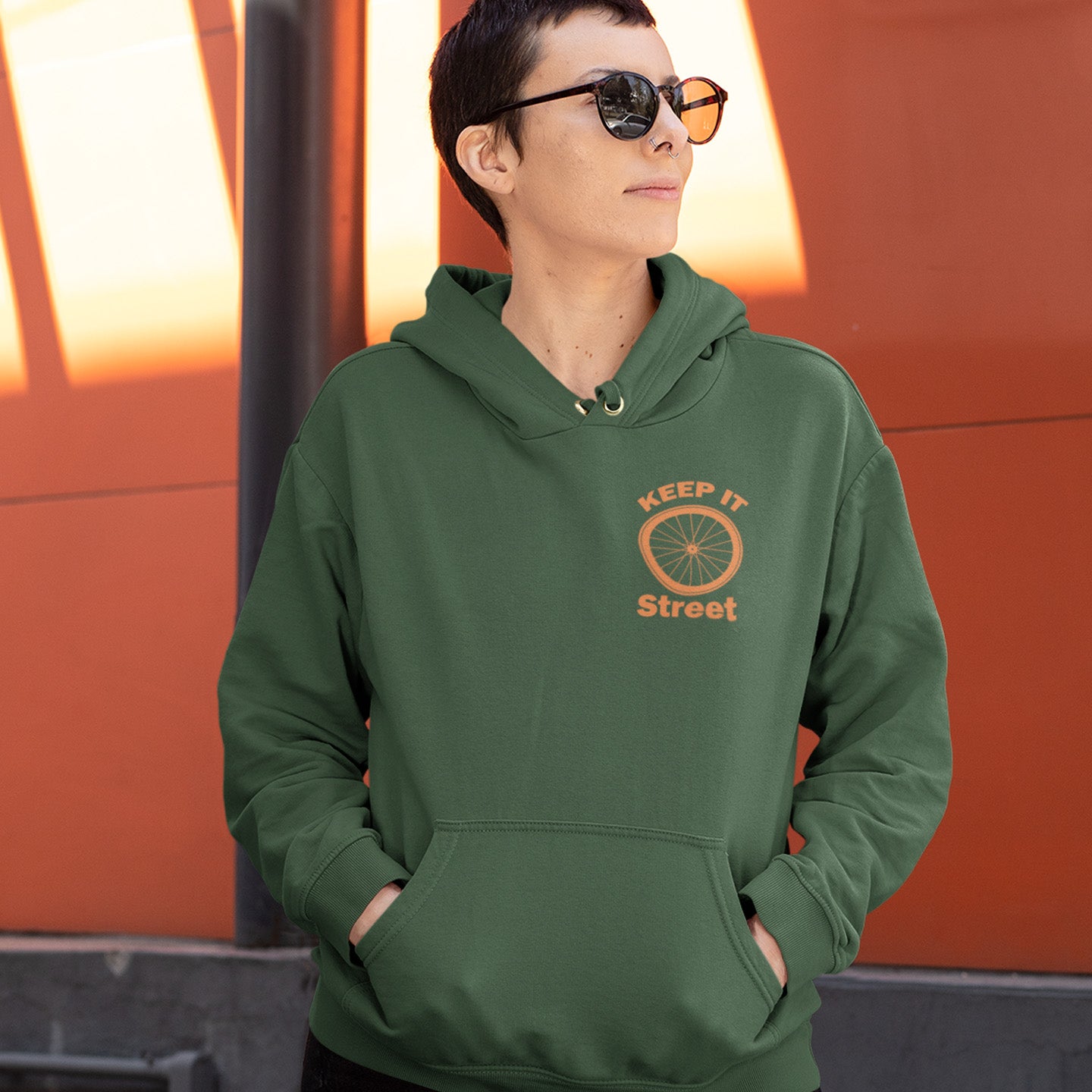 Person wearing a green hoodie with 'Keep It Street' logo against an orange background. This street art inspired hoodie design represents inner city street life as a culture of it's own.  Wherever you are in the world, may the street be with you. Comfortable and practical. It's extra soft and has a convenient front pouch pocket. Made from organic cotton and recycled polyester, this street art hoodie is a great eco-friendly choice.