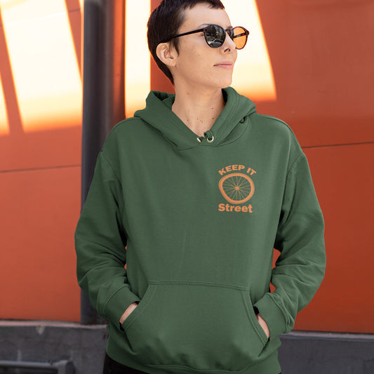 Person wearing a green hoodie with 'Keep It Street' logo against an orange background. This street art inspired hoodie design represents inner city street life as a culture of it's own.  Wherever you are in the world, may the street be with you. Comfortable and practical. It's extra soft and has a convenient front pouch pocket. Made from organic cotton and recycled polyester, this street art hoodie is a great eco-friendly choice.
