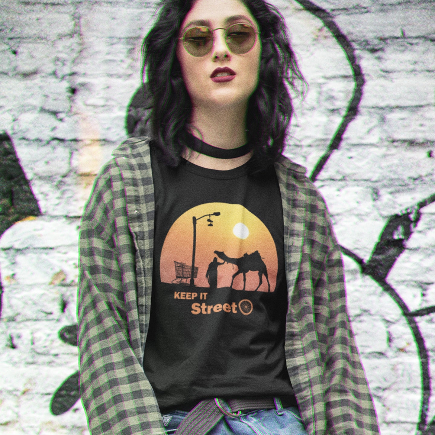 Person wearing a black t-shirt with  text, standing against a graffiti-covered wall. This humorous, underground stencil art represents inner city street life as a culture of it's own. There is a ground level reality mixed with trustworthy honestly at street level in towns and cities across the planet. Wherever you are in the world, may the street be with you. Made from 100% organic ring-spun cotton, this street art t-shirt is unisex, high-quality, super comfy, and best of all, eco-friendly.