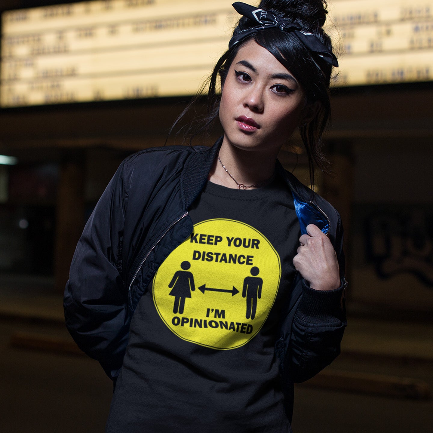 Person wearing a black jacket with a yellow graphic and text, standing against a blurred indoor background. This opinionated t shirt design is a warning to people who speak before they think. It's best to warn them before they try to treat you like a clone. Made from 100% organic ring-spun cotton, this urban art t shirt is unisex, high-quality, super comfy, and best of all, eco-friendly.