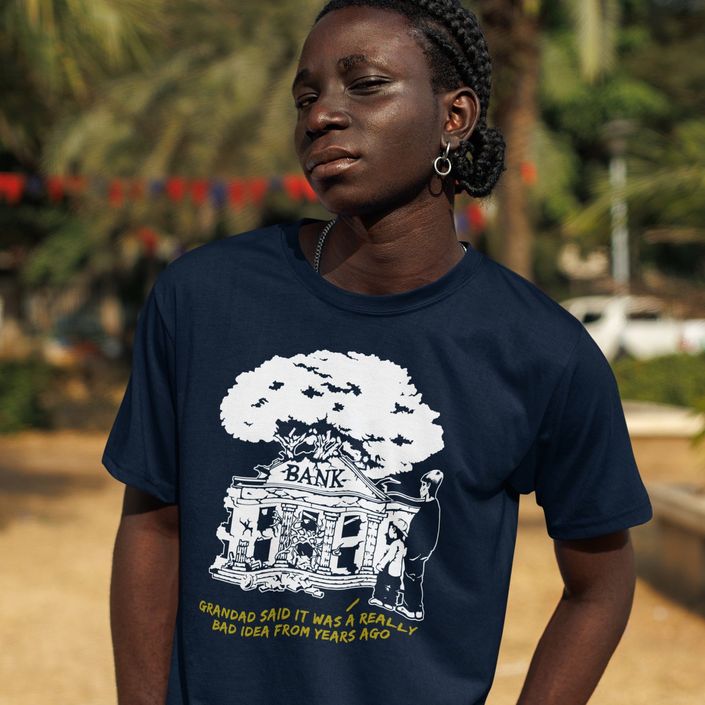 Person wearing a French navy blue t-shirt with a graphic design and text outdoors. An anti capitalism t shirt with a wishful message. A thought provoking future where money and banking are a dark memory and our children have something more natural to look forward to. Made from 100% organic ring-spun cotton, this utopian graffiti stencil t-shirt is unisex, high-quality, super comfy, and best of all, eco-friendly.