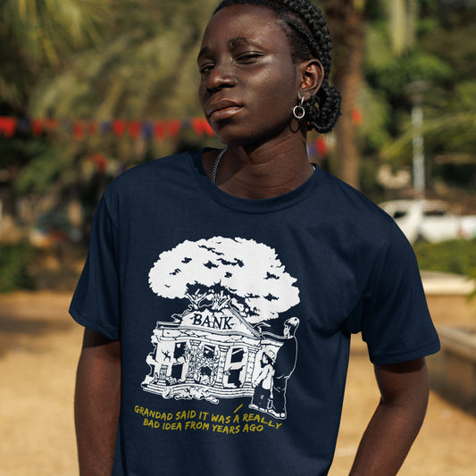 Person wearing a French navy blue t-shirt with a graphic design and text outdoors. An anti capitalism t shirt with a wishful message. A thought provoking future where money and banking are a dark memory and our children have something more natural to look forward to. Made from 100% organic ring-spun cotton, this utopian graffiti stencil t-shirt is unisex, high-quality, super comfy, and best of all, eco-friendly.