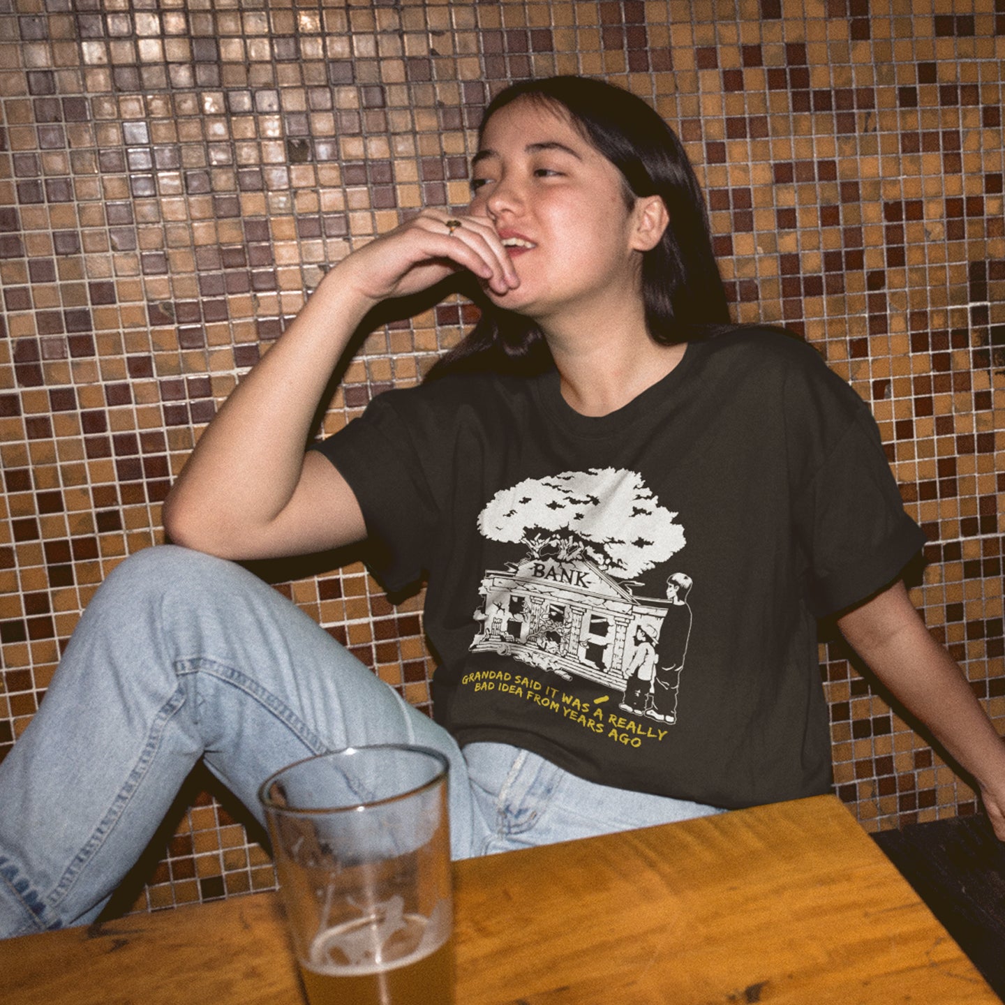 Person sitting at a table with a glass of beer, wearing a black t-shirt with a graphic design. An anti capitalism t shirt with a wishful message. A thought provoking future where money and banking are a dark memory and our children have something more natural to look forward to. Made from 100% organic ring-spun cotton, this utopian graffiti stencil t-shirt is unisex, high-quality, super comfy, and best of all, eco-friendly.