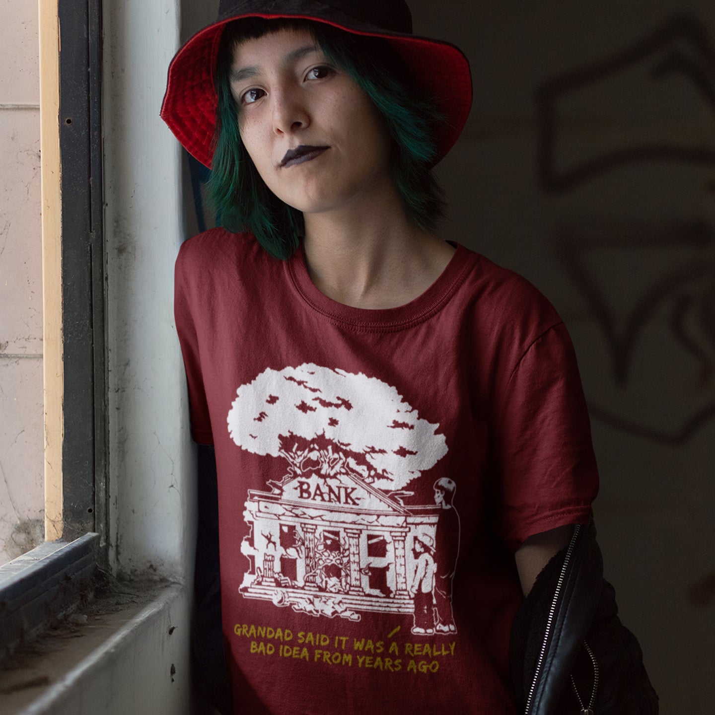 Person wearing a burgundy t-shirt with a graphic design and text, standing indoors. An anti capitalism t shirt with a wishful message. A thought provoking future where money and banking are a dark memory and our children have something more natural to look forward to. Made from 100% organic ring-spun cotton, this utopian graffiti stencil t-shirt is unisex, high-quality, super comfy, and best of all, eco-friendly.