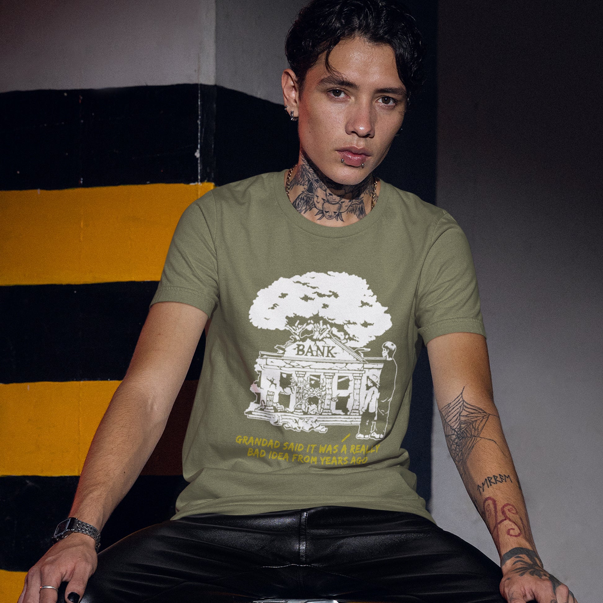 Person wearing a khaki t-shirt with a graphic design sitting against a striped wall. An anti capitalism t shirt with a wishful message. A thought provoking future where money and banking are a dark memory and our children have something more natural to look forward to. Made from 100% organic ring-spun cotton, this utopian graffiti stencil t-shirt is unisex, high-quality, super comfy, and best of all, eco-friendly.