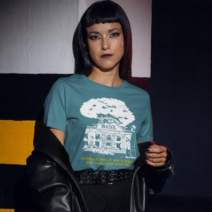 Woman wearing a stargazer t-shirt with a graphic design, sitting against a colourful wall. An anti capitalism t shirt with a wishful message. A thought provoking future where money and banking are a dark memory and our children have something more natural to look forward to. Made from 100% organic ring-spun cotton, this utopian graffiti stencil t-shirt is unisex, high-quality, super comfy, and best of all, eco-friendly.