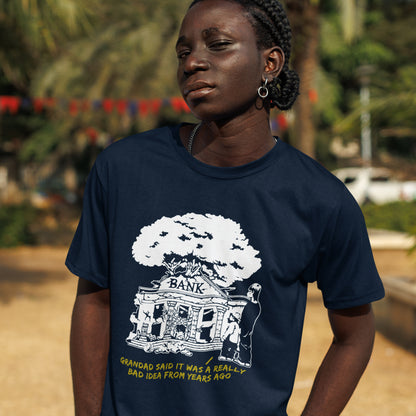 Person wearing a navy blue t-shirt with a graphic design and text. A Banksy style stencil art t-shirt with an anti-capitalism message. A thought provoking future where money and banking are a dark memory and our children have something more natural to look forward to. Made from 100% organic ring-spun cotton, this utopian graffiti stencil t-shirt is unisex, high-quality, super comfy, and best of all, eco-friendly.