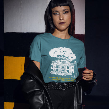 Person wearing a teal t-shirt with a graphic design sitting against a colourful wall. A Banksy style stencil art t-shirt with an anti-capitalism message. A thought provoking future where money and banking are a dark memory and our children have something more natural to look forward to. Made from 100% organic ring-spun cotton, this utopian graffiti stencil t-shirt is unisex, high-quality, super comfy, and best of all, eco-friendly.