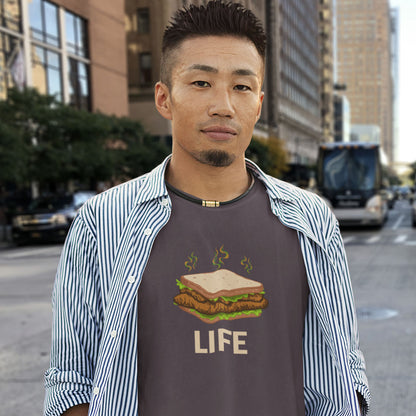 A man wearing a dark brown graphic t-shirt with a sandwich illustration and the word 'LIFE' printed on the front, styled with an open blue and white striped button-down shirt, standing on a city street.