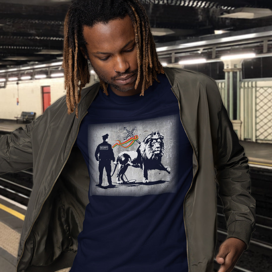 A man with dreadlocks standing in a tube station, wearing a French navy blue  crew neck t-shirt with a graffiti stencil design of a security guard checking the underside of the Lion of Judah for explosives.