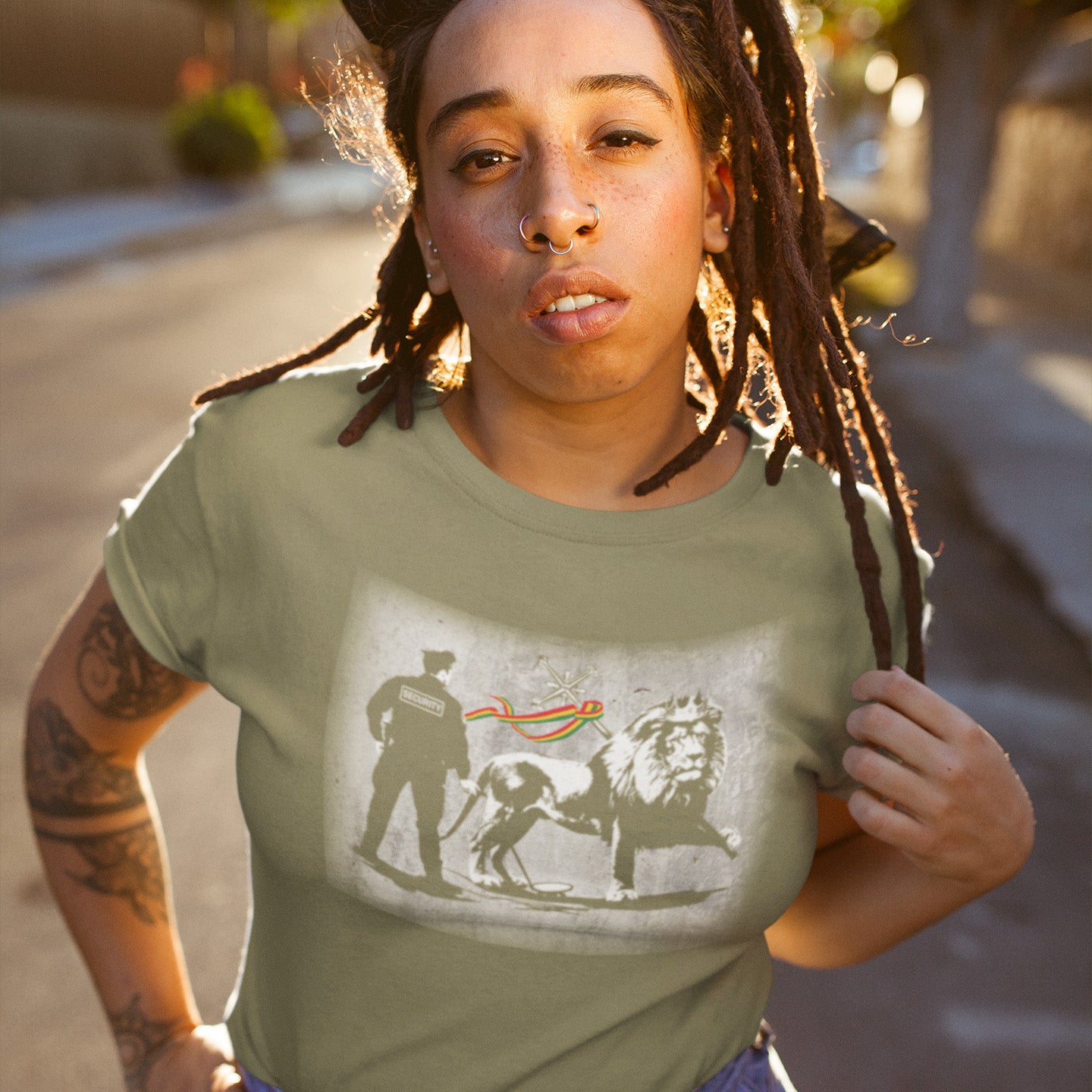 Person wearing a Khaki t-shirt with a graphic design outdoors. A stencil graffiti t shirt design mocking how much security we have in the western world, from a Rastafarian view point. Made from 100% organic ring-spun cotton, this urban art t shirt is unisex, high-quality, super comfy, and best of all, eco-friendly.