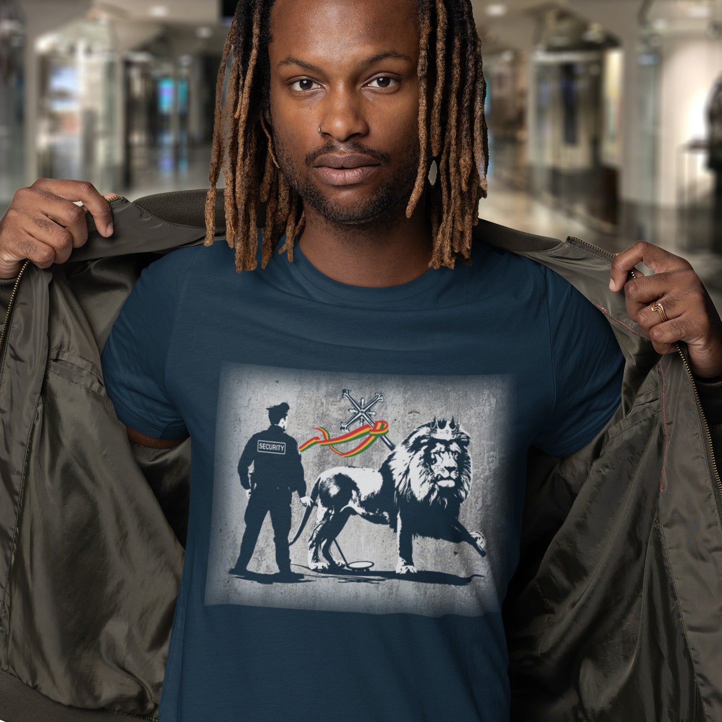 Man wearing a navy blue t-shirt with a graphic design in an indoor setting. A Banksy style t-shirt in a stencil art mockery of how much security we have in the western world, from a Rastafarian view point. Made from 100% organic ring-spun cotton, this graffiti stencil art t-shirt is unisex, high-quality, super comfy, and best of all, eco-friendly.