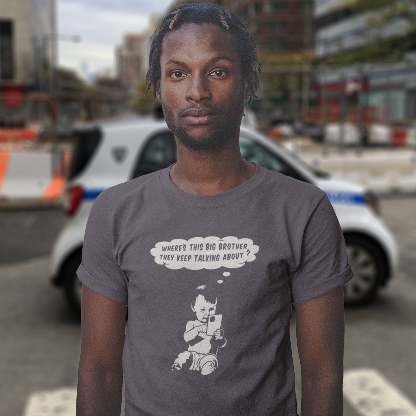 Person wearing a t-shirt with a graphic and text, standing in an urban setting. A witty conspiracy theory t-shirt questioning the existence of a controlling 'Big Brother' watching over us. This unique design in stencil art illustrates the sweet mind of a child and a lesson in how to take things literally. Big Brother is everywhere and nowhere. Made from 100% organic ring-spun cotton, this Banksy style conspiracy theory t-shirt is unisex, high-quality, super comfy, and best of all, eco-friendly.