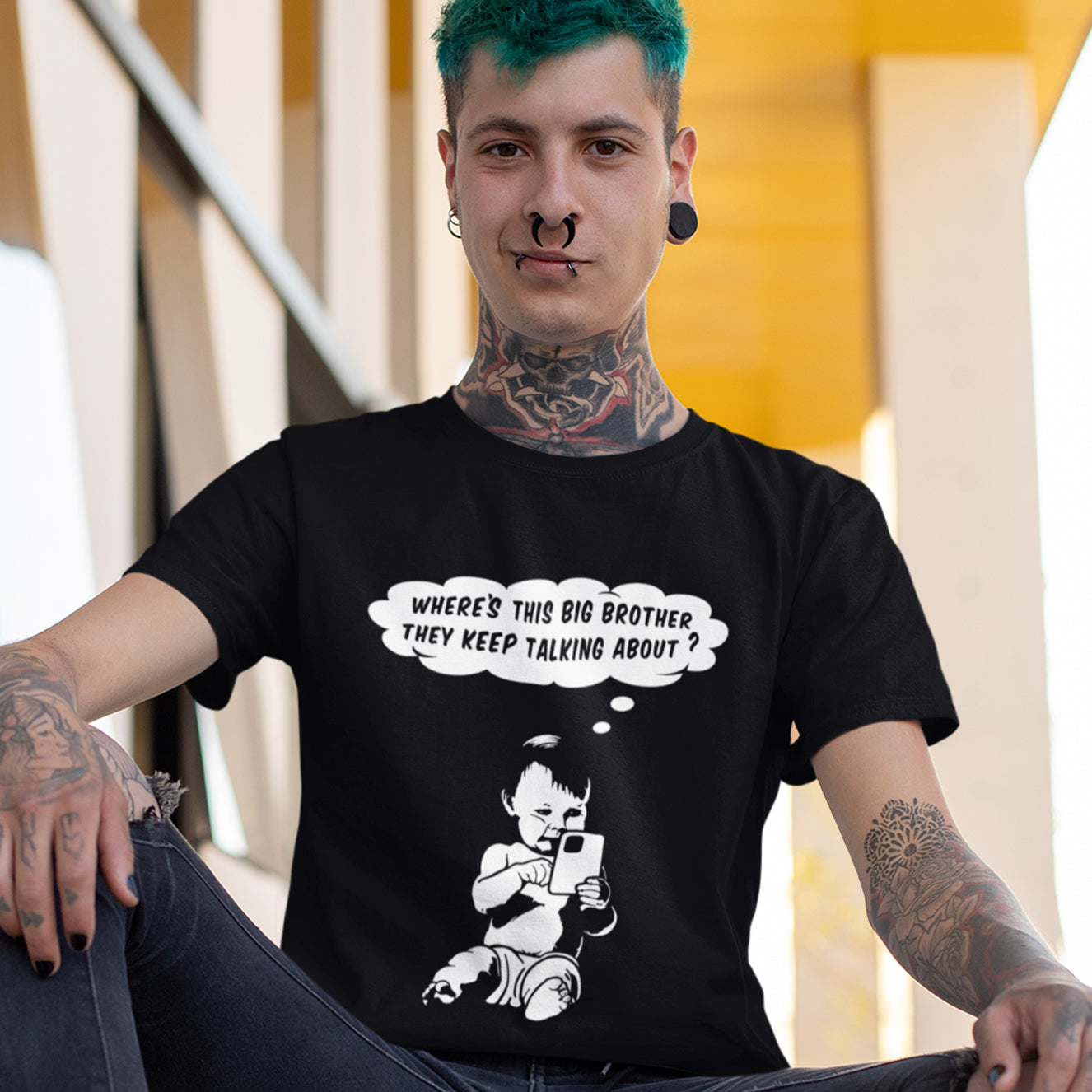Person wearing a black t-shirt with a graphic and text, sitting outdoors. A witty conspiracy theory t-shirt questioning the existence of a controlling 'Big Brother' watching over us. This unique design in stencil art illustrates the sweet mind of a child and a lesson in how to take things literally. Big Brother is everywhere and nowhere. Made from 100% organic ring-spun cotton, this Banksy style conspiracy theory t-shirt is unisex, high-quality, super comfy, and best of all, eco-friendly.
