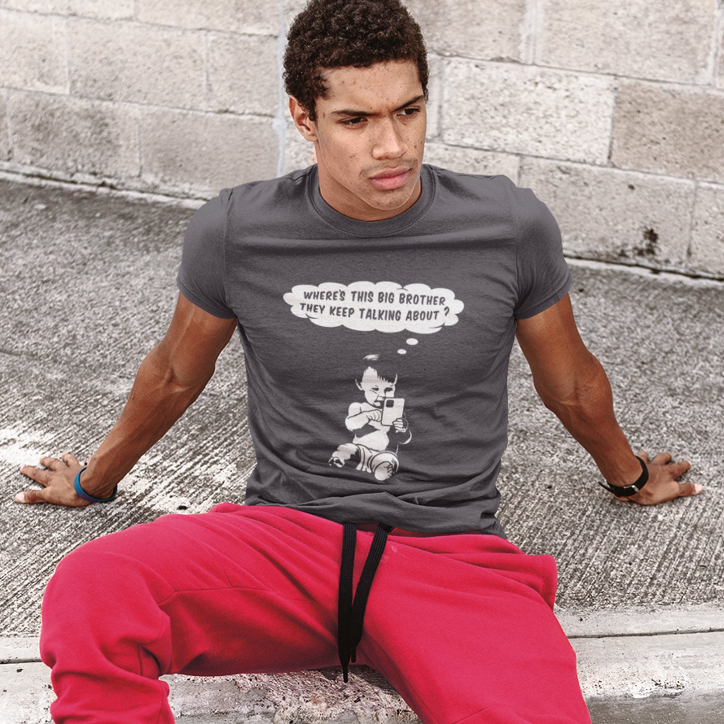 Person wearing an anthracite t-shirt with a graphic design sitting on a concrete surface. A funny conspiracy theory t shirt questioning the existence of a controlling 'Big Brother' watching over us. This unique design in stencil art illustrates the sweet mind of a child and a lesson in how to take things literally. Big Brother is everywhere and nowhere. Made from 100% organic ring-spun cotton, this stencil graffiti t shirt is unisex, high-quality, super comfy, and best of all, eco-friendly.