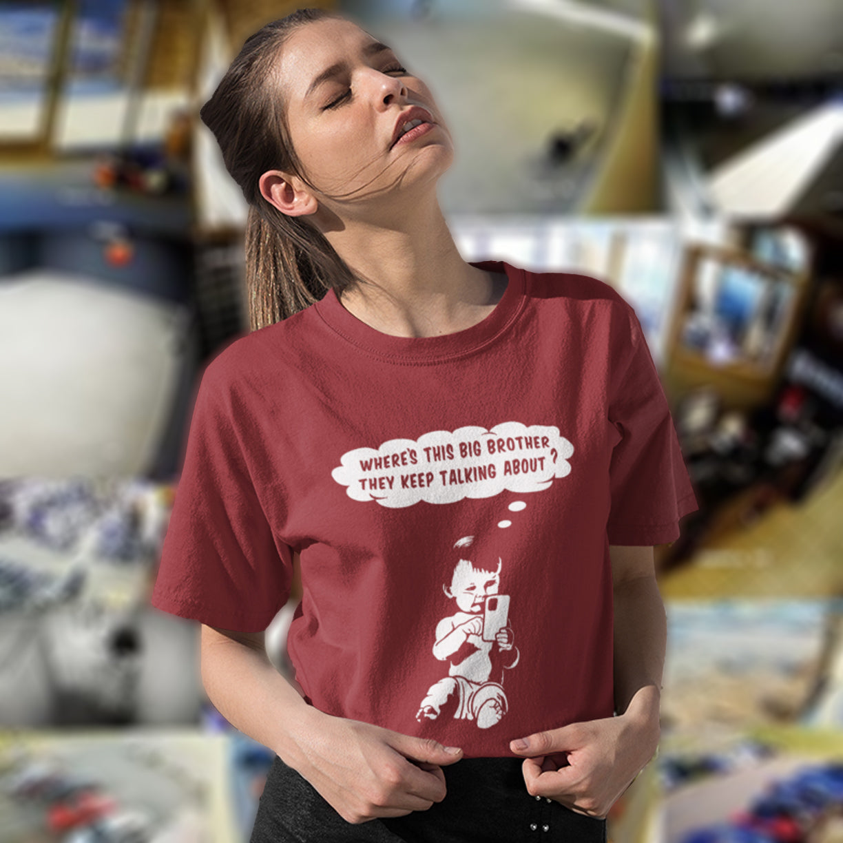 Person wearing a burgundy t-shirt with a graphic and text in a store setting. A funny conspiracy theory t shirt questioning the existence of a controlling 'Big Brother' watching over us. This unique design in stencil art illustrates the sweet mind of a child and a lesson in how to take things literally. Big Brother is everywhere and nowhere. Made from 100% organic ring-spun cotton, this stencil graffiti t shirt is unisex, high-quality, super comfy, and best of all, eco-friendly.