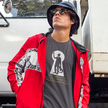 A man wearing a red hooded jacket with black and white graphic panels and an anthracite grey graphic t-shirt with a white graphic features a white keyhole silhouette of a reptilian salesman holding his hat, with gold text underneath reading 'SORRY TO BOTHER YOU BUT COULD I INTEREST YOU IN A RELIABLE CONSPIRACY THEORY?'.