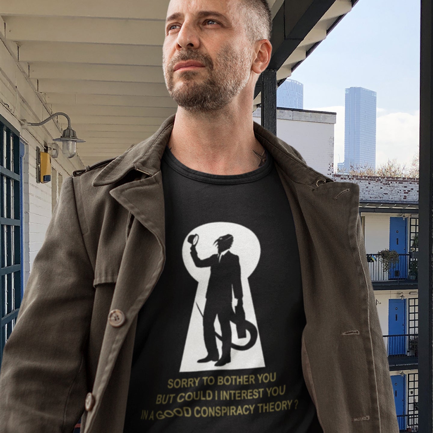 Man wearing a black t-shirt with a graphic design and text, standing outdoors. A funny conspiracy theory t-shirt. Just an ordinary, everyday, door-to-door conspiracy theory salesman. Made from 100% organic ring-spun cotton, this reptilian alien t-shirt is unisex, high-quality, super comfy, and best of all, eco-friendly.