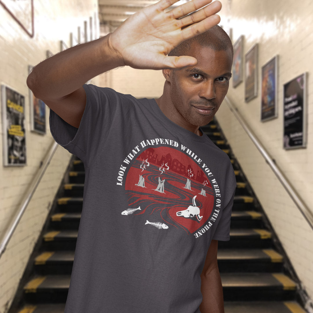 Man wearing a t-shirt with a graphic design in an indoor setting. An anti mobile phone abuse theme mixed with a save the earth t shirt. This design is a harsh view of what's happening to the planet while people are distracted by their phones. Made from 100% organic ring-spun cotton, this save the planet t shirt is unisex, high quality, super comfy, and best of all, eco-friendly.