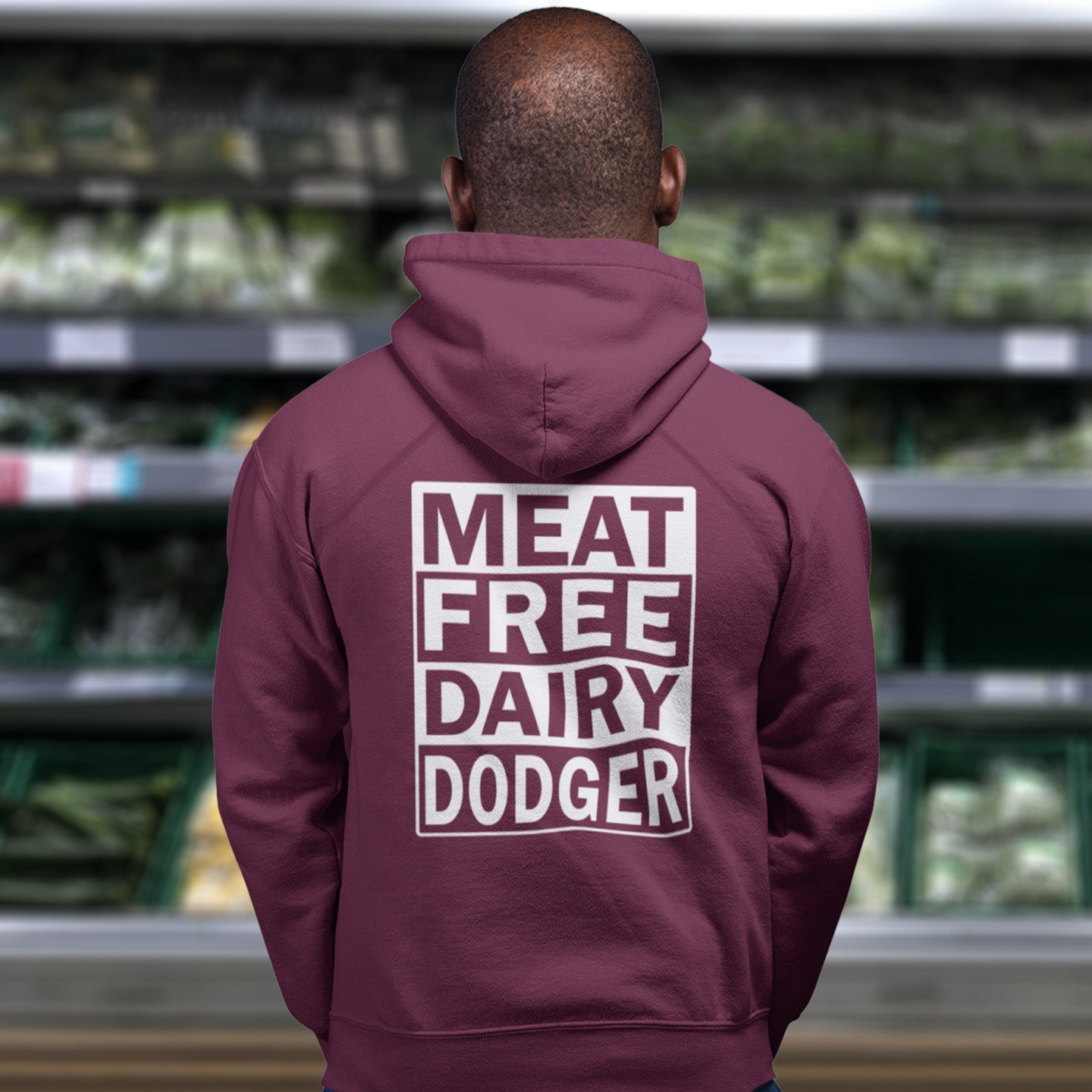 Person wearing a burgundy hoodie with 'MEAT FREE DAIRY DODGER' text in a grocery store. This plant based vegan hoodie promotes a witty alternative to the 'non-dairy' label. Never mind 'plant based' as a new label for vegan . This is straight off the streets of East London. Comfortable and practical. It's extra soft and has a convenient front pouch pocket. Made from organic cotton and recycled polyester, this meat free hoodie design is a great eco-friendly choice.