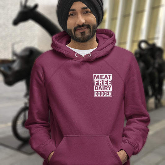 Person wearing a burgundy hoodie with 'MEAT FREE DAIRY DODGER' text, standing in an urban setting. This vegan hoodie promotes a witty alternative to the 'non-dairy' label. Never mind 'plant based' as a new label for vegan . This is straight off the streets of East London. Comfortable and practical. It's extra soft and has a convenient front pouch pocket. Made from organic cotton and recycled polyester, this vegan hoodie is a great eco-friendly choice.