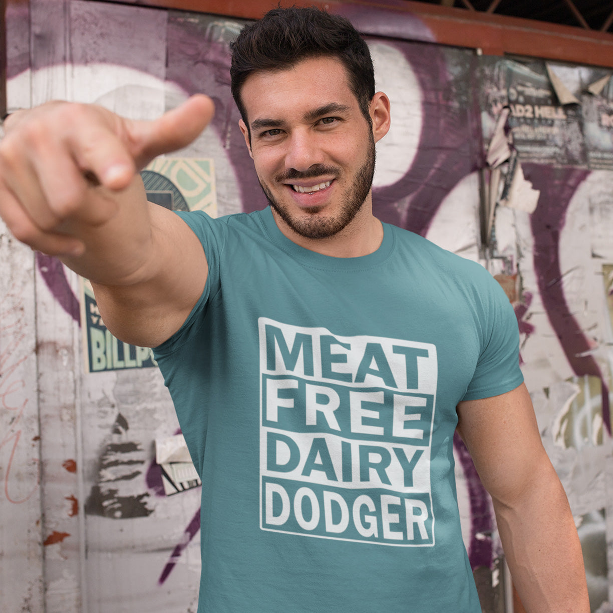Man wearing a 'MEAT FREE DAIRY DODGER' t-shirt pointing towards the camera with a colourful mural in the background. A vegan meat free t shirt promoting a witty alternative to the 'vegan' label. Never mind 'plant based' as a new label for vegan . This is straight off the streets of East London. Made from 100% organic ring-spun cotton, this vegan dairy free t shirt is unisex, high-quality, super comfy, and best of all, eco-friendly.