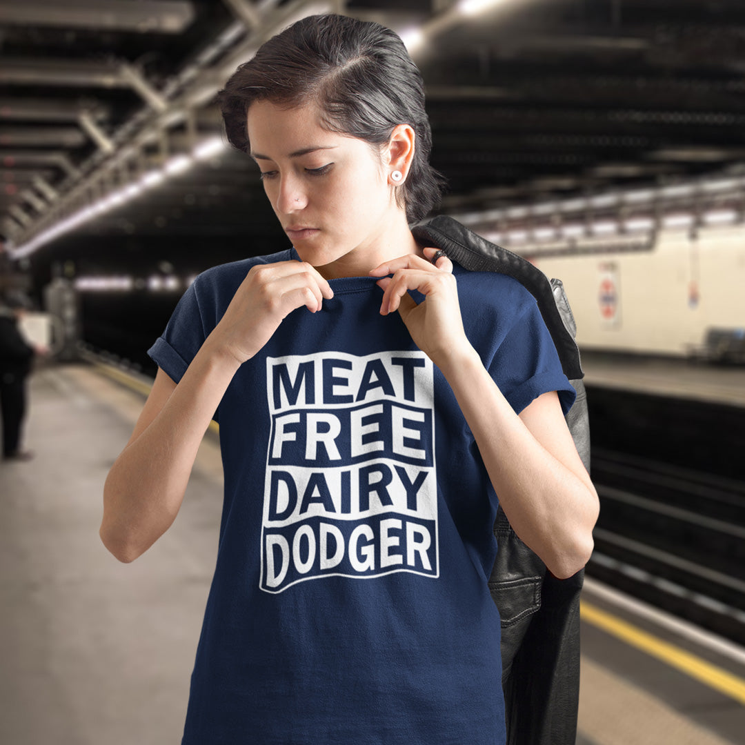 A woman wearing a French navy blue t-shirt with 'MEAT FREE DAIRY DODGER' printed in white block letters, standing on a train station platform with a black jacket slouched over her shoulder.