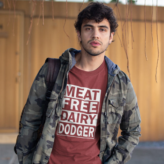 A man wearing a burgundy graphic t-shirt with the text 'MEAT FREE DAIRY DODGER' in white, layered under an open camouflage jacket, standing outdoors against a wooden wall.