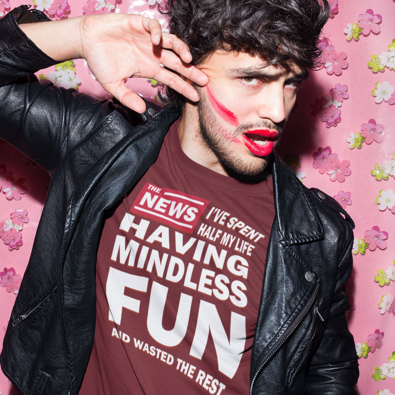 Man wearing a leather jacket and a t-shirt with text, posing against a pink floral background. A witty quotes t shirt with a front page life philosophy. When you look back over your life, How are you going to see it ? Made from 100% organic ring-spun cotton, these clever slogan t shirts are unisex, high-quality, super comfy, and best of all, eco-friendly.
