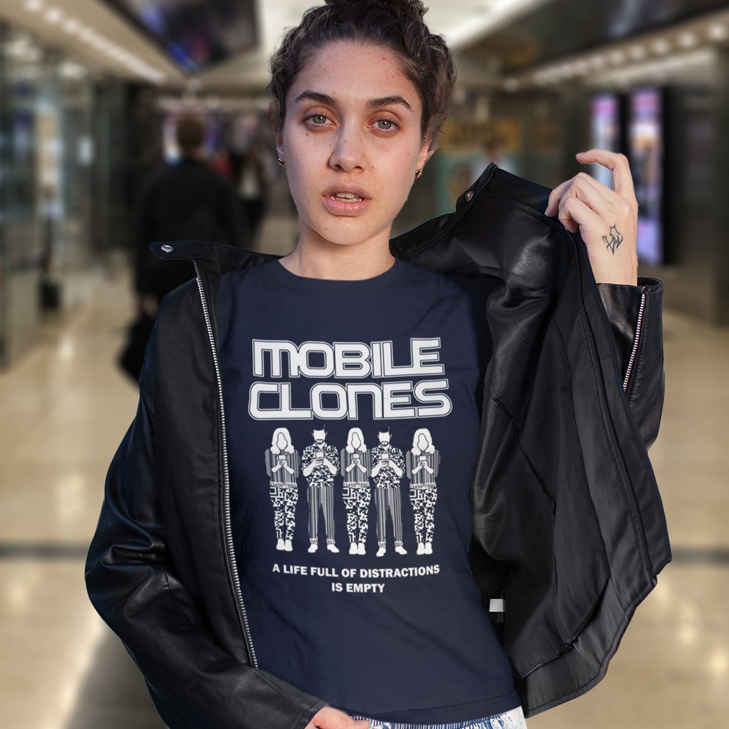 Person wearing a black jacket and a t-shirt with 'MOBILE CLONES' design in a mall setting. This anti mobile phone abuse t shirt design is encouraging social awareness of the distraction from important issues that the mobile phone creates, especially with consumerism.  Made from 100% organic ring-spun cotton, this anti-consumerism t shirt is unisex, high-quality, super comfy, and best of all, eco-friendly.