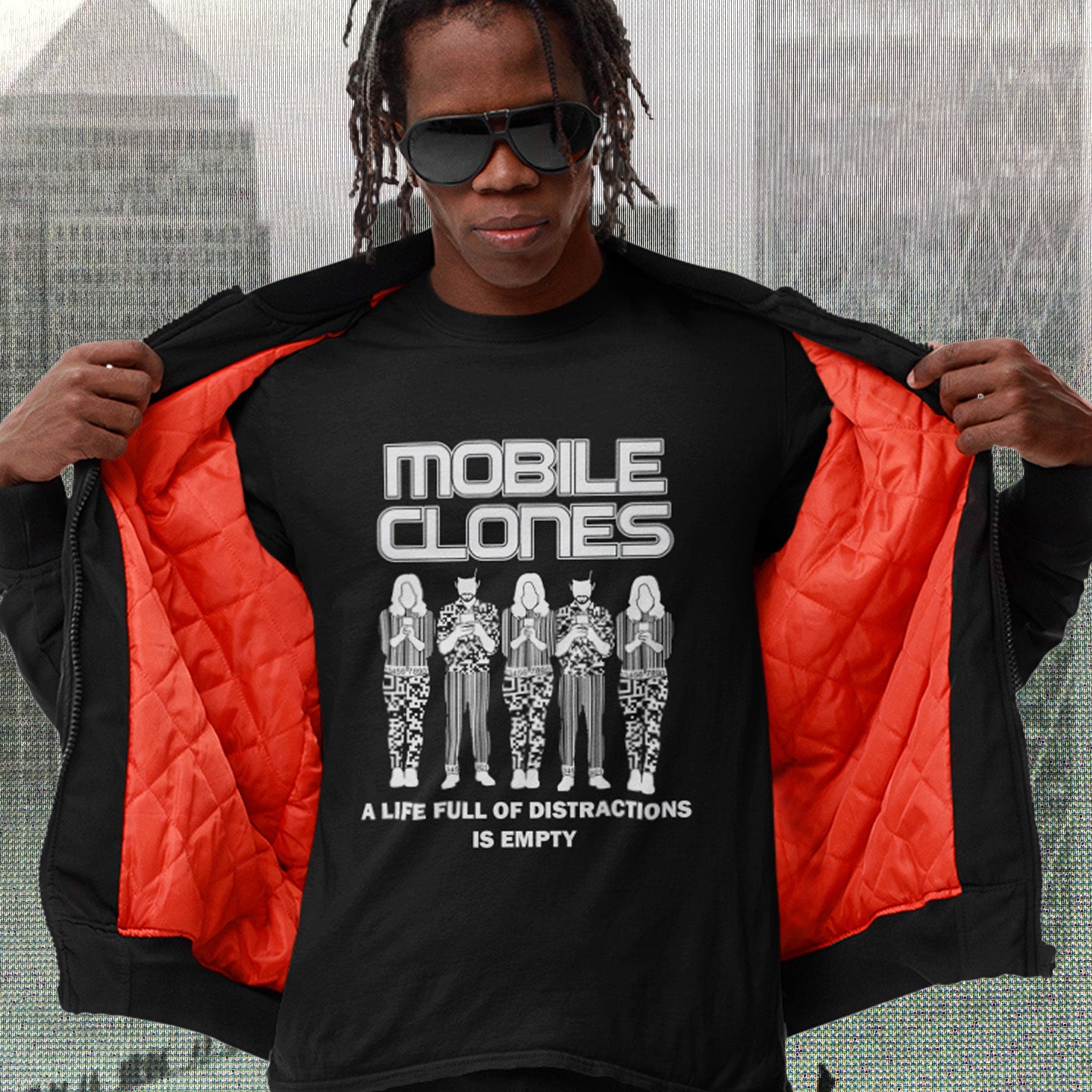 Person wearing a black t-shirt with 'Mobile Clones' design and red jacket, cityscape background. Smart phones are taking the imagination out of life. Soon we will all look the same, think the same, and all buy the same un-needed online products, or has that already happened ? Made from 100% organic ring-spun cotton, this anti-consumerism t-shirt is unisex, high-quality, super comfy, and best of all, eco-friendly.