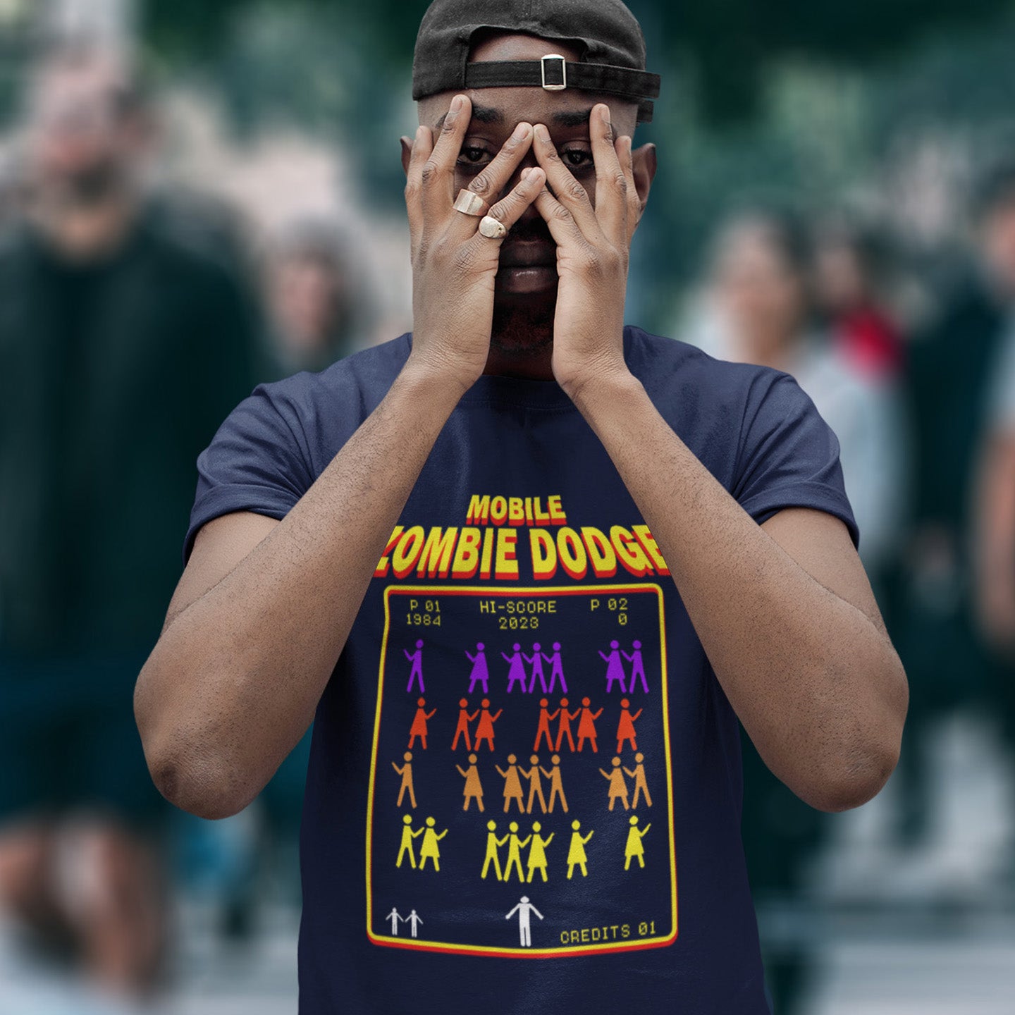 Person wearing a t-shirt with 'Mobile Zombie Dodge' design in a crowd. A satirical gamer t-shirt design for anyone who feels they are in a repetitive 80's video game every time they enter a crowded street scene. Welcome to the age of the mobile phone and lack of social awareness. Made from 100% organic ring-spun cotton, this unisex gamer t-shirt is alternative and original. It's high-quality, super comfy, and best of all—eco-friendly.