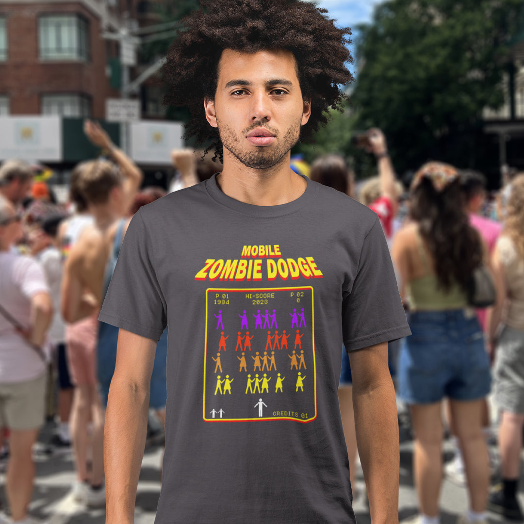 A man wearing an anthracite grey graphic t-shirt with a 'Mobile Zombie Dodge' print, standing in a blurred outdoor crowd scene.